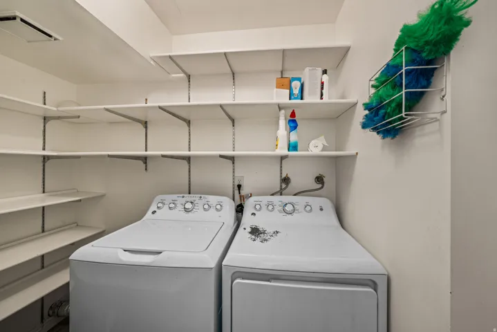 Dedicated utility space featuring a washer and dryer, extensive wall-mounted shelving, and white walls