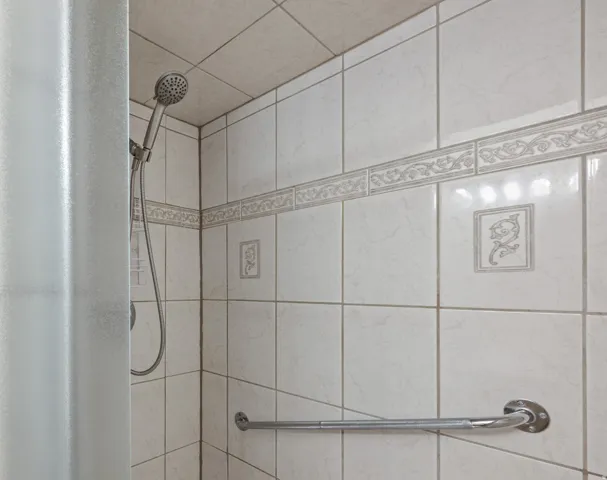 Tiled shower stall featuring a handheld showerhead, decorative accent tiles, and a chrome grab bar