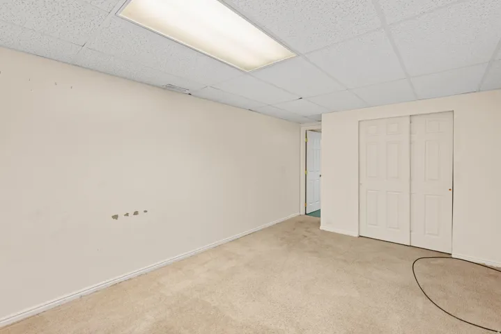 Carpeted room featuring a drop ceiling with integrated fluorescent lighting, white walls, and white baseboards