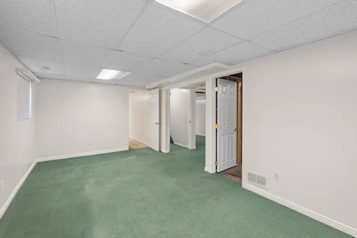 Room featuring green carpeting, white walls, and a drop ceiling with recessed lighting