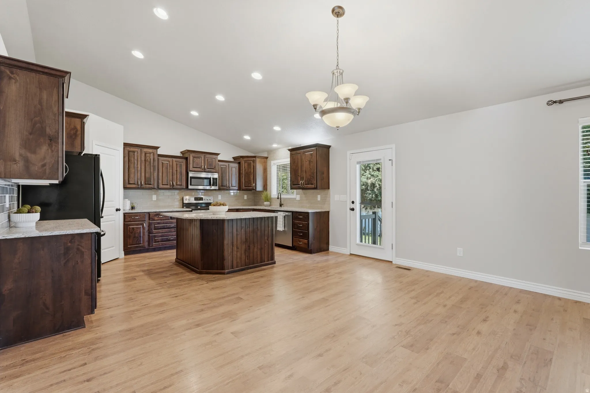 Spacious kitchen featuring rich wood cabinetry, stainless steel appliances, a central island with countertop seating, recessed lighting, and light wood-finish flooring