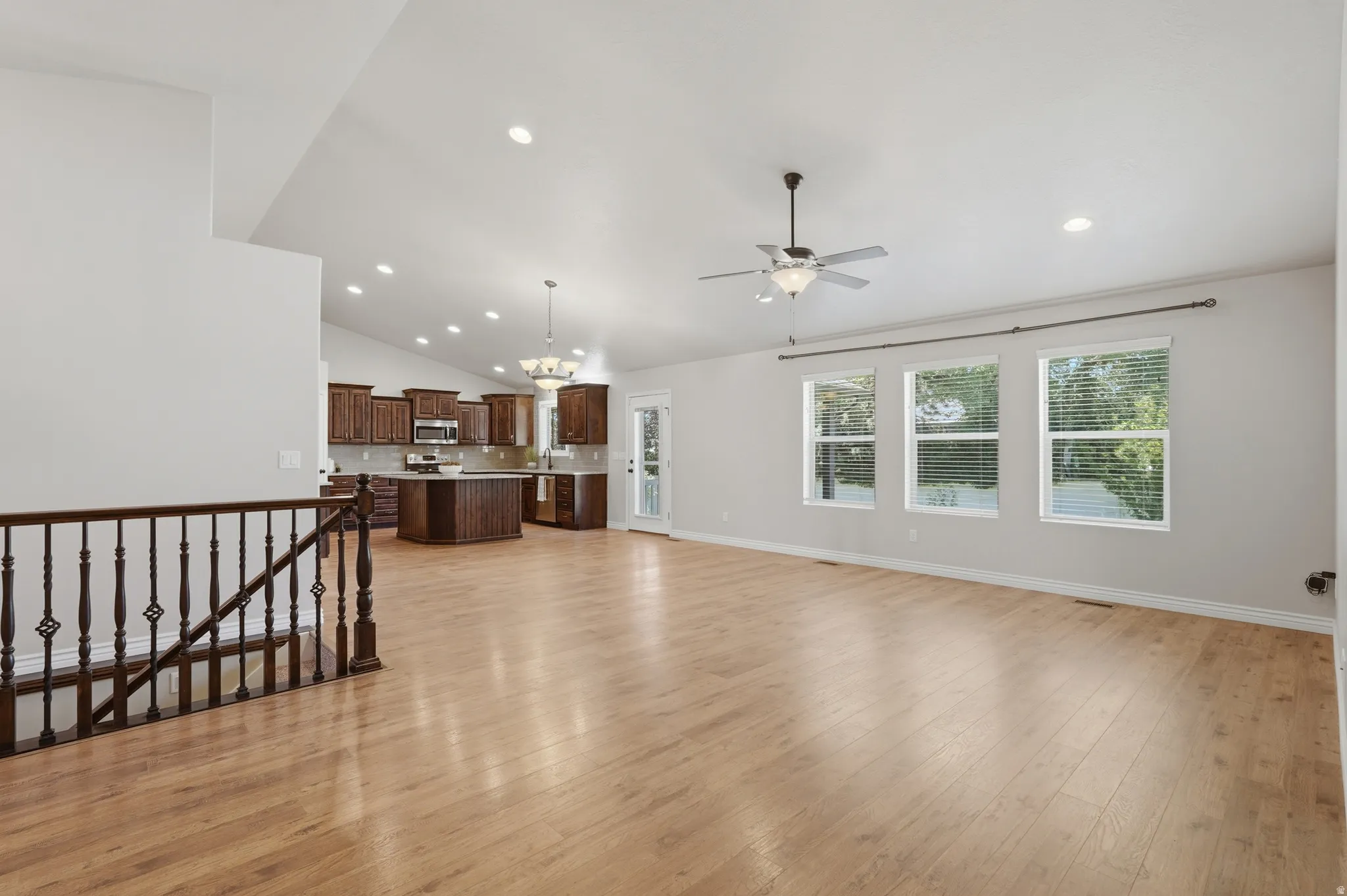 Open-concept living space featuring wood-finish flooring, vaulted ceilings with recessed lighting, and a kitchen with dark wood cabinetry