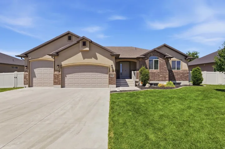 Front exterior featuring a stucco and brick facade, a two-car garage, a concrete driveway, a manicured lawn, and a white privacy fence