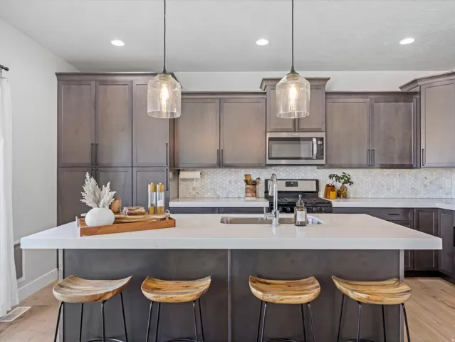 Kitchen featuring a large island with a sink, pendant lighting, stainless steel appliances, a hex tile backsplash, and extensive cabinetry