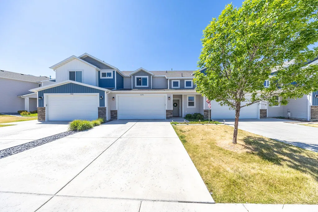Townhome exterior featuring blue and white siding, stone accents, two single-car garages, and a concrete driveway