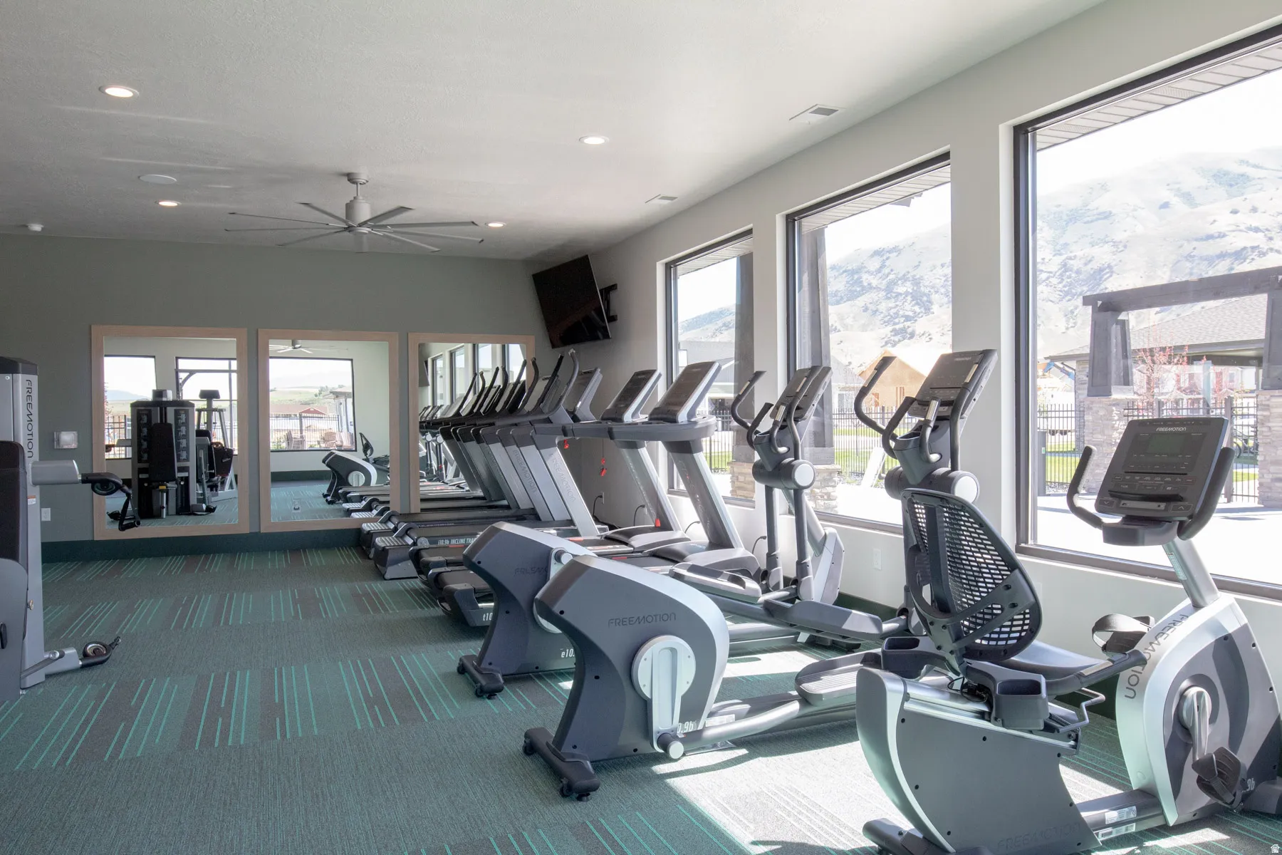 Fitness center featuring cardio equipment, strength training machines, integrated televisions, ceiling fan, and large windows with mountain scenery