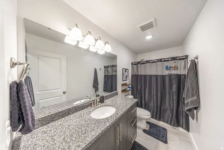 Bathroom featuring a spacious vanity with a light speckled countertop, an undermount sink, and a large wall-mounted mirror