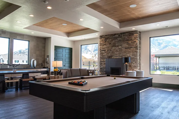 Spacious entertainment room featuring wood-finish flooring, a stone accent wall with a built-in fireplace, and large windows