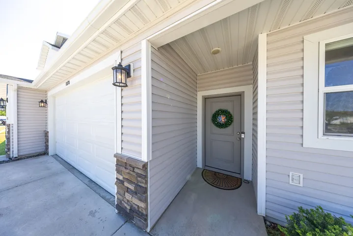 Exterior featuring light gray horizontal siding, an attached garage with a white panel door, a covered entry with a recessed light, and stone veneer accents
