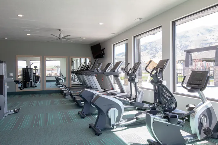 Fitness center featuring cardio equipment, strength training machines, integrated televisions, ceiling fan, and large windows with mountain scenery