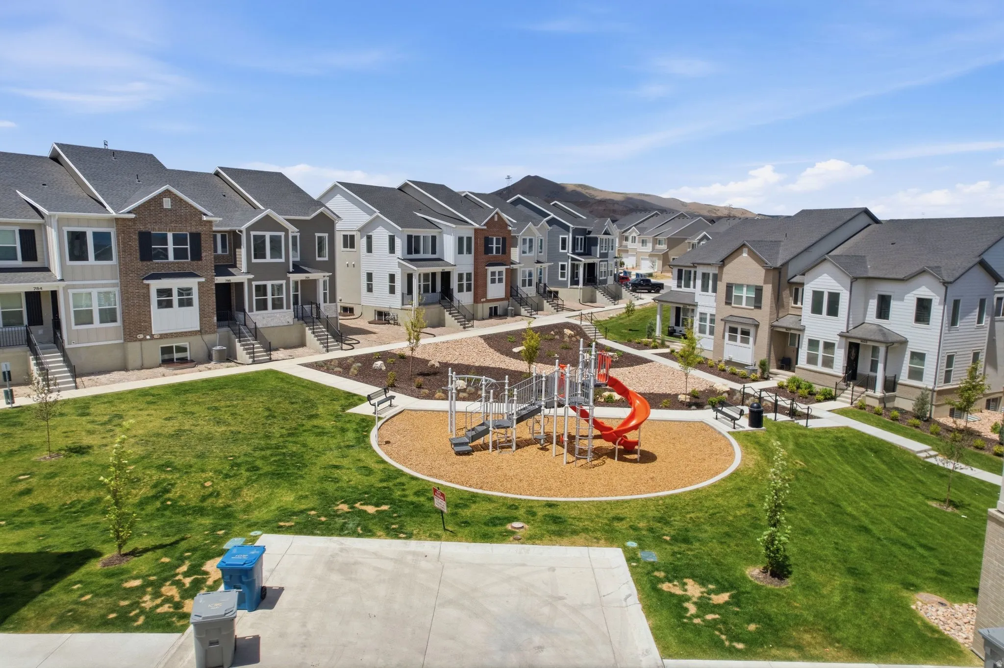 Central green space with playground equipment, surrounded by multi-story townhomes, paved pathways, and mature landscaping