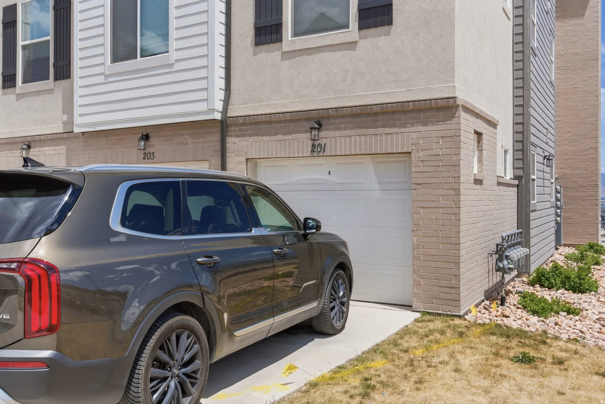 Exterior featuring a one-car garage, brick veneer, stucco siding, horizontal siding, and an asphalt driveway
