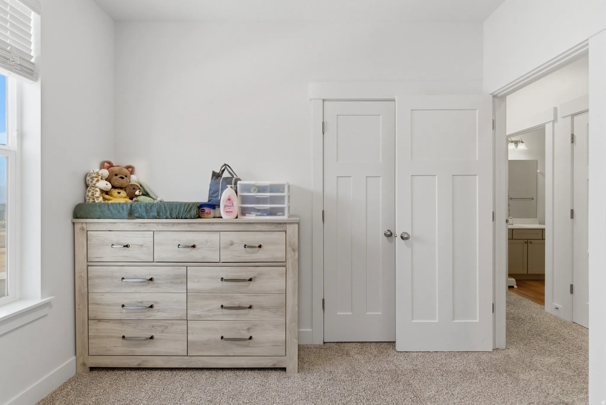 Bright interior space featuring a window with white blinds, neutral carpeting, and white walls