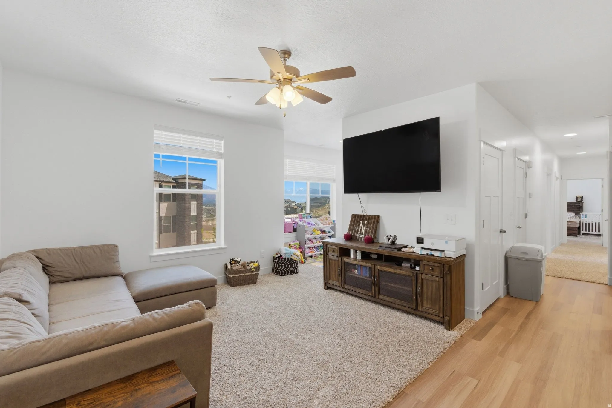 Spacious living area featuring neutral carpeting, a ceiling fan with integrated lighting, and multiple windows
