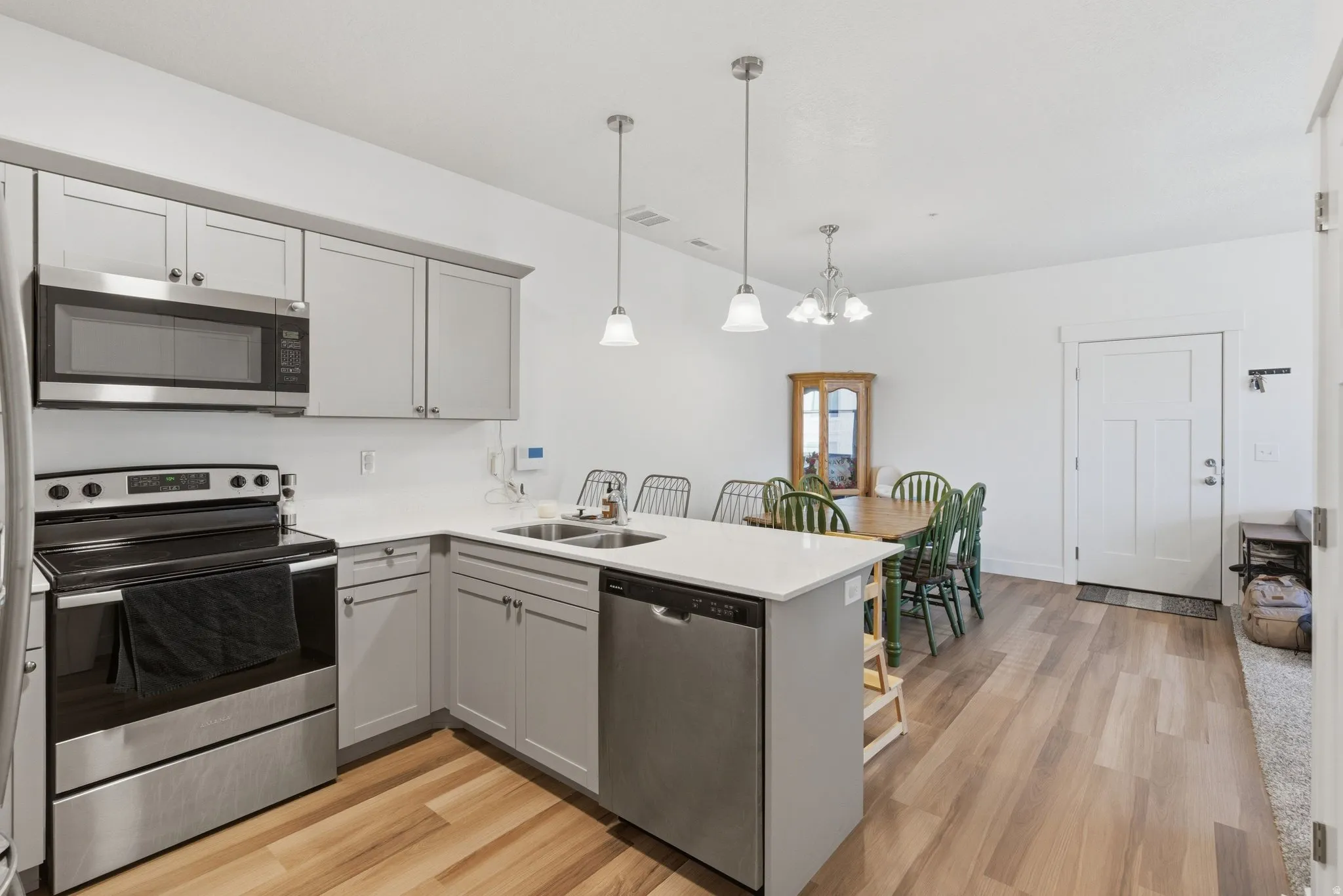 Modern kitchen featuring light gray cabinetry, stainless steel appliances, a white countertop, and wood-finish flooring