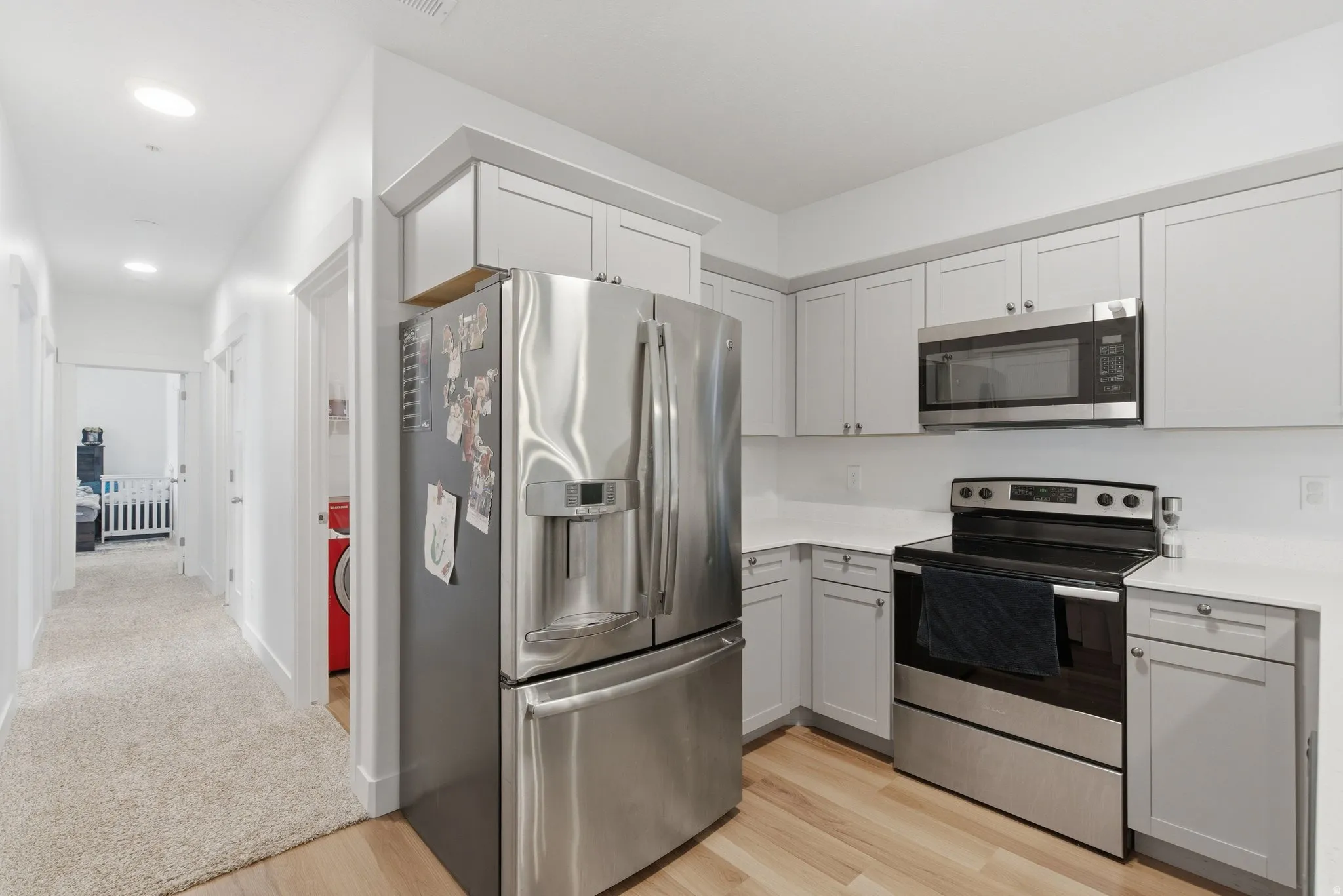 Modern kitchen featuring light gray cabinetry, stainless steel appliances, white countertops, and wood-finish flooring