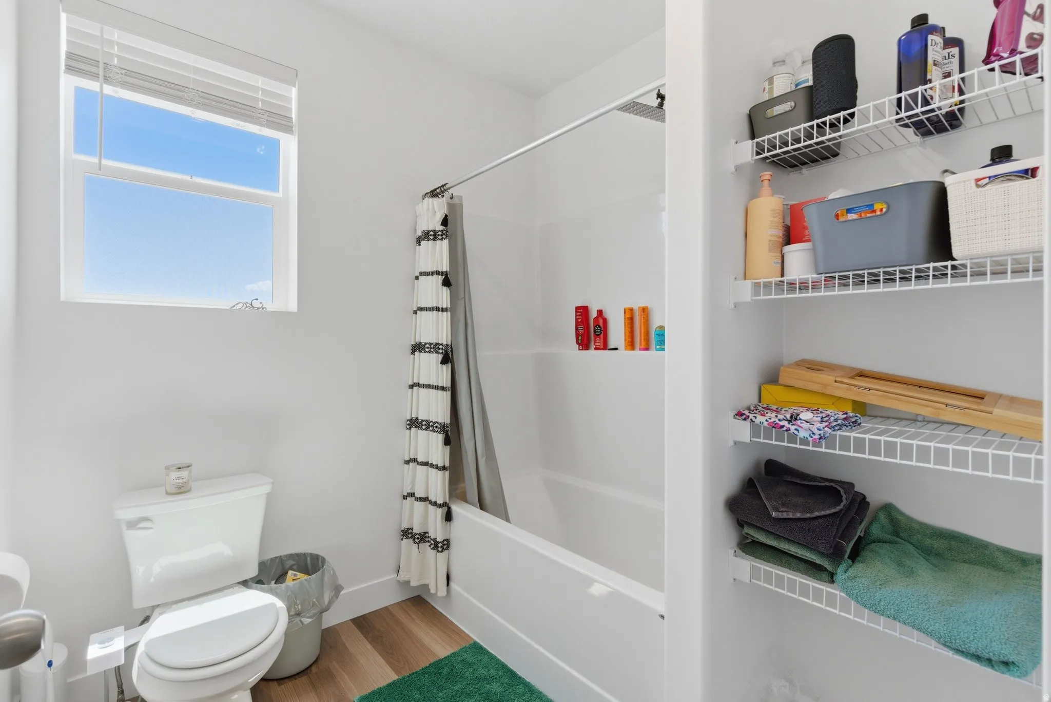 Full bath with a tub/shower combination, window, toilet, and built-in wire shelving
