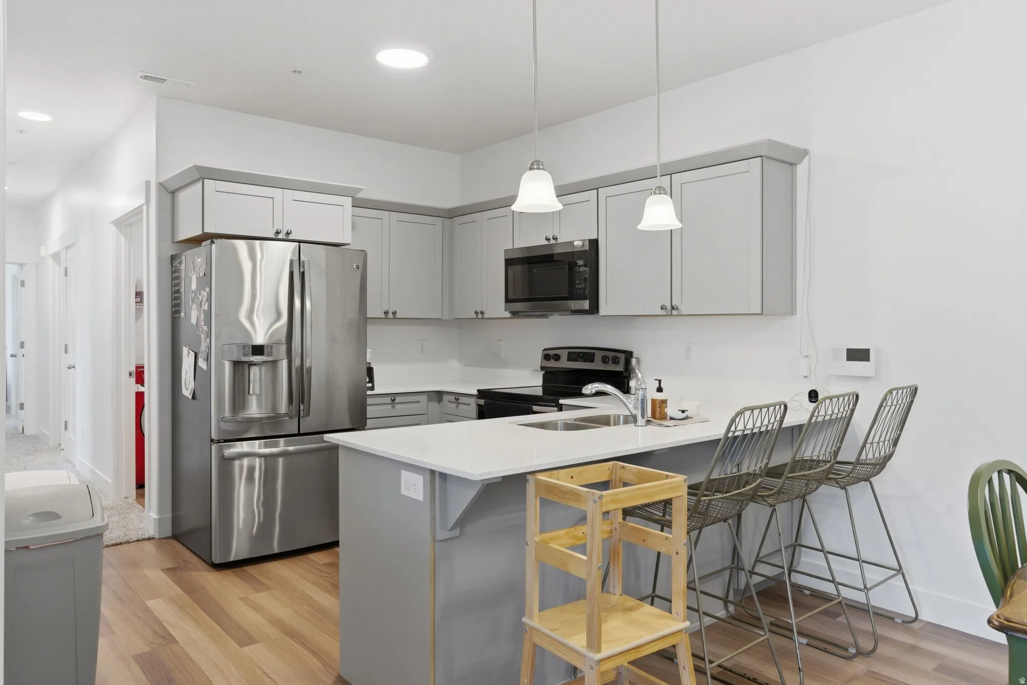 Kitchen featuring light wood-finish flooring, gray perimeter cabinetry, a central island with countertop seating, stainless steel appliances, and pendant lighting