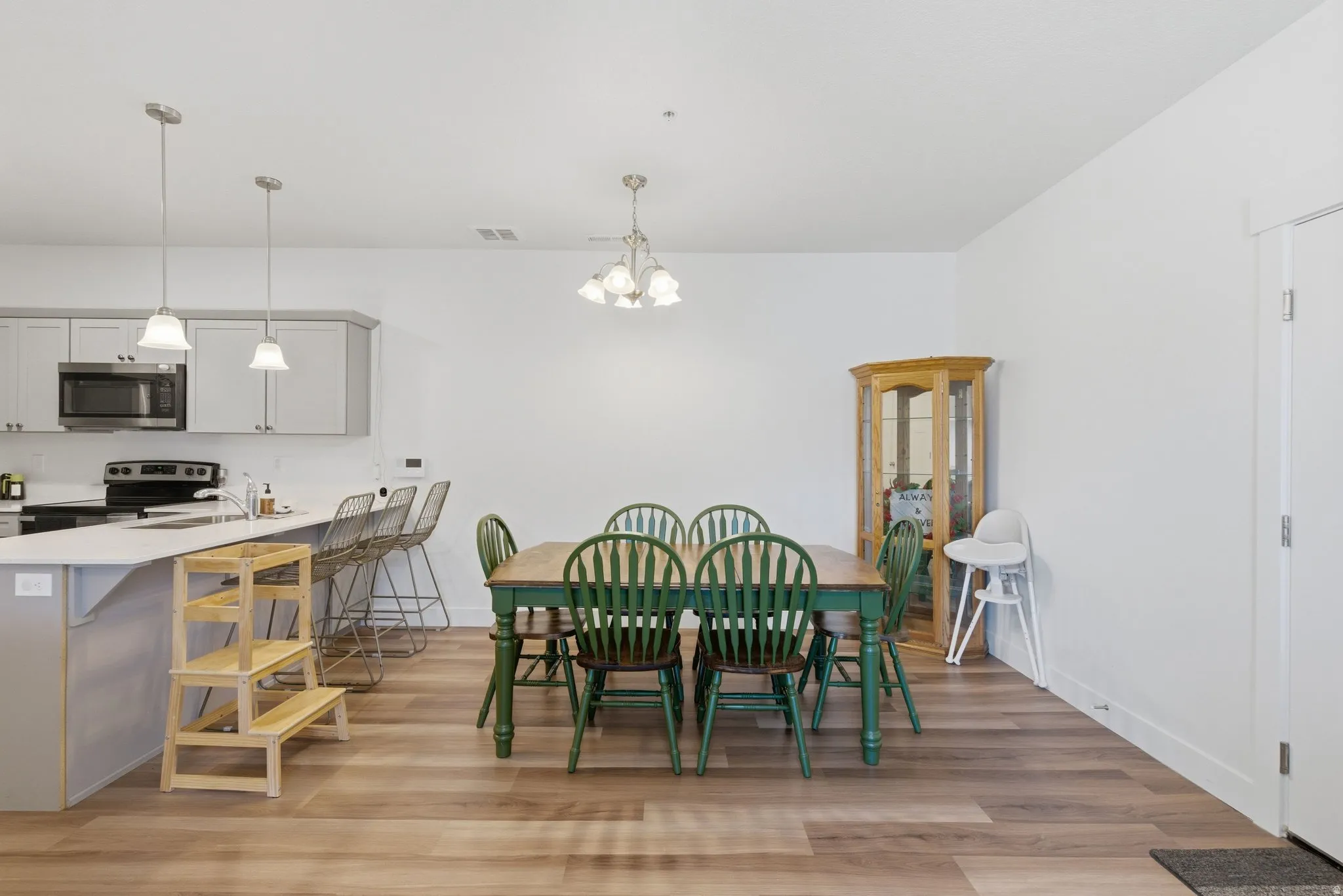 Open-concept kitchen and dining area featuring wood-finish flooring, light grey cabinetry, stainless steel appliances, and a kitchen island with pendant lighting