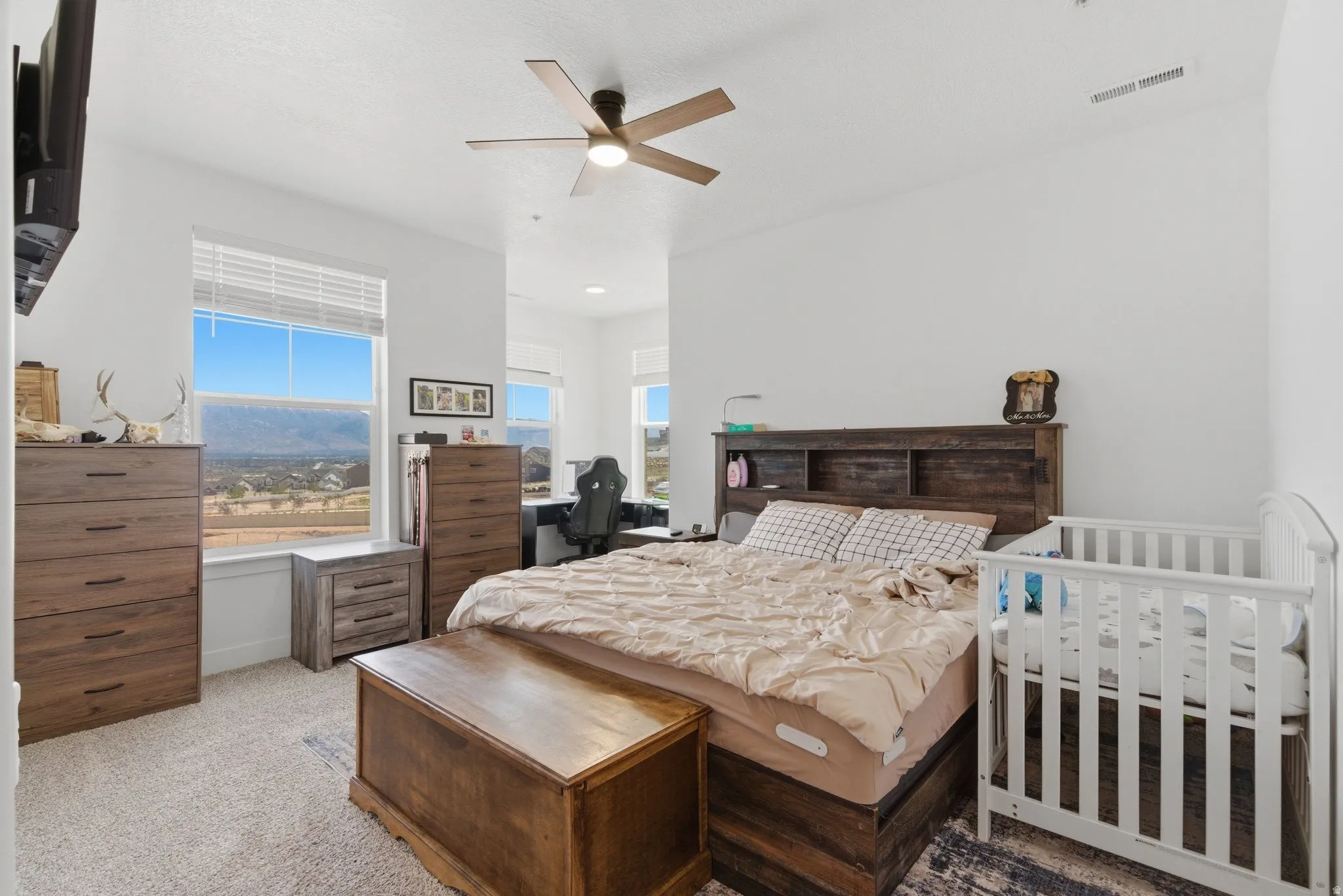 Spacious room with large windows, light-colored walls, a ceiling fan, and carpeted flooring