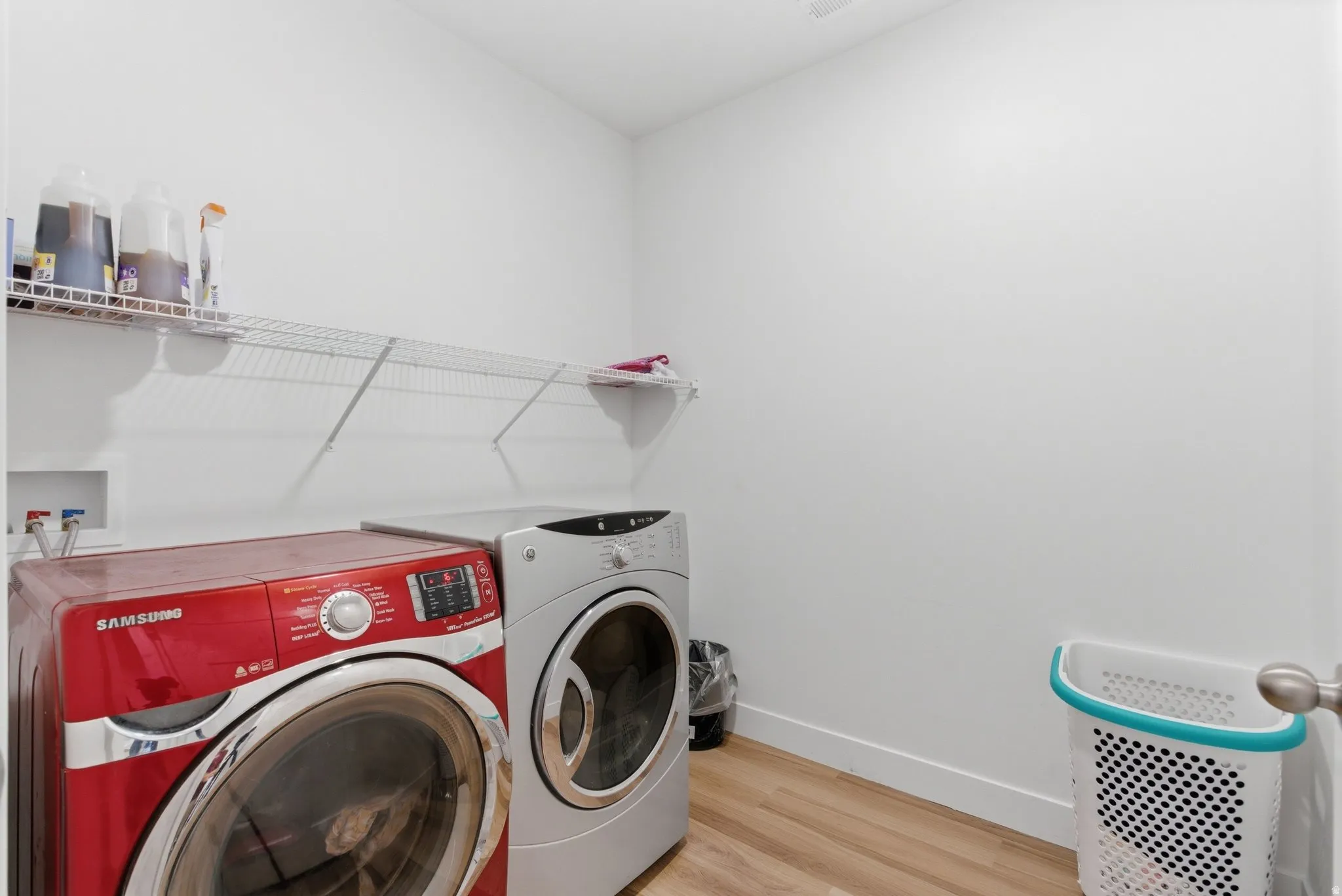 Dedicated laundry area featuring white walls, wood-finish flooring, and wire shelving for organization