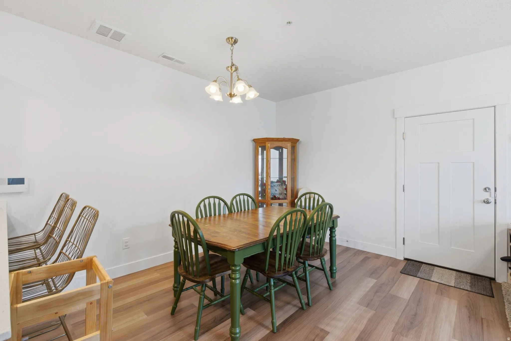 Open concept dining area with light wood-finish flooring, white walls, and a contemporary chandelier