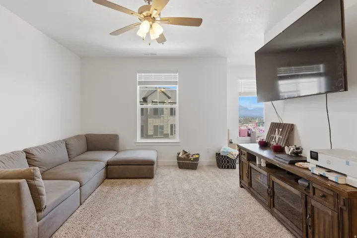 Spacious room with light-colored carpet flooring, a ceiling fan with integrated lighting, and white walls