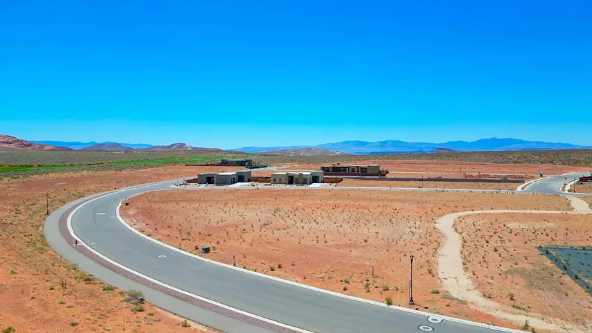 Expansive desert landscape featuring a paved road, undeveloped land, and distant residential structures