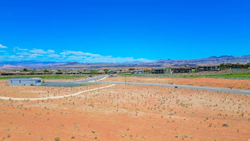 Expansive undeveloped land featuring a paved road, dirt paths, and distant residential structures