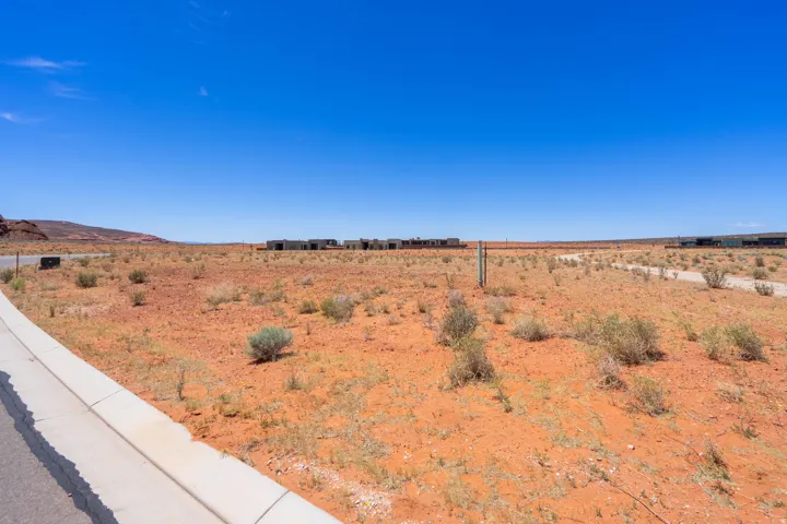 Expansive undeveloped lot featuring a paved road, concrete curb, and desert landscape