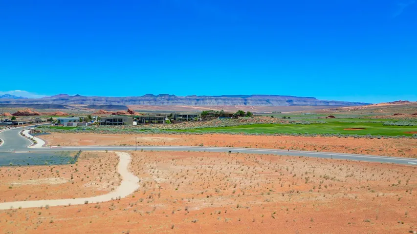 Expansive desert landscape featuring a paved road, winding dirt path, and distant residential structures
