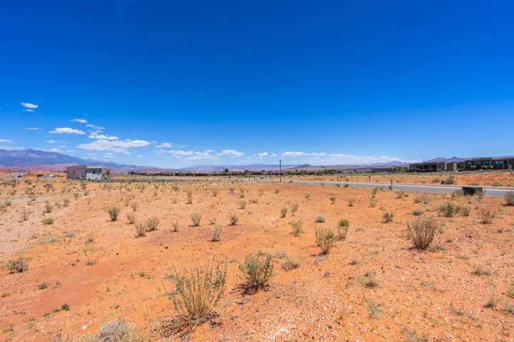 Expansive desert landscape featuring red soil and scattered low-lying vegetation