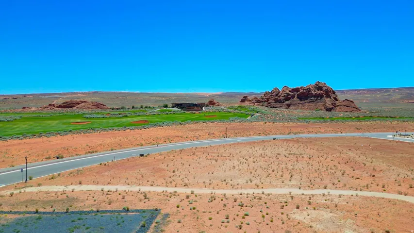 Expansive desert lot featuring a paved road, scattered vegetation, and distant green golf course elements