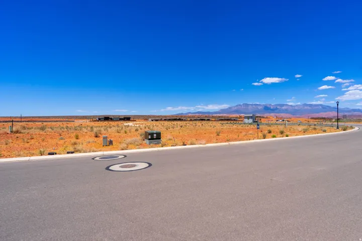 Paved roadway bordering a desert landscape with distant mountains