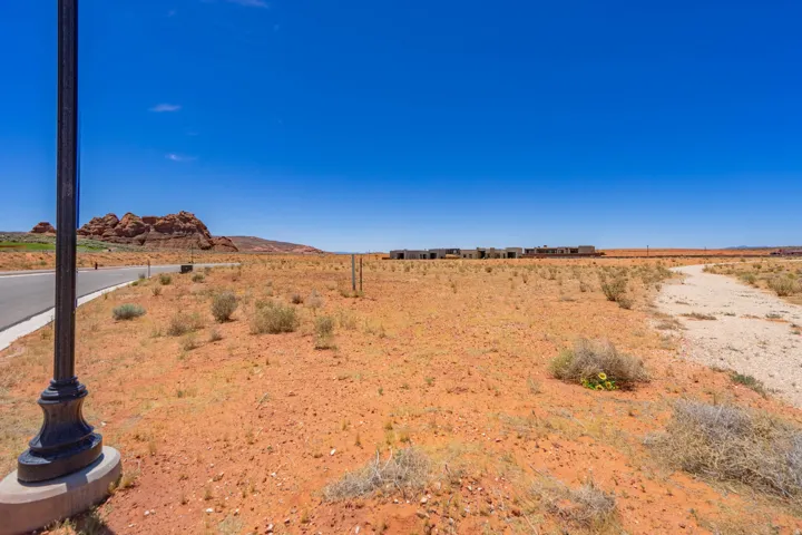 Expansive undeveloped land featuring a paved road, a light post with a concrete base, and distant rock formations