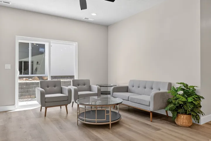 Spacious room featuring wood-finish flooring, a contemporary ceiling fan, recessed lighting, and a sliding glass door opening to an exterior rock and block retaining wall