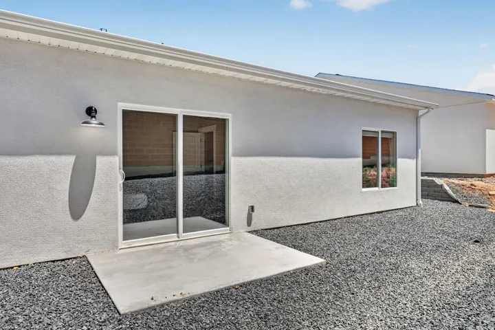 Rear exterior featuring a sliding glass door, concrete patio, single window, and gravel landscaping