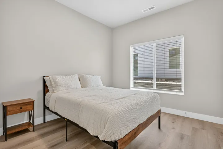 Spacious room featuring light wood-finish flooring, a large window with horizontal blinds, neutral wall paint, white trim, and a ceiling vent