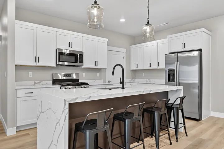 Kitchen featuring an island with waterfall edge, stainless steel appliances, white cabinetry, a black matte faucet, and wood-finish flooring