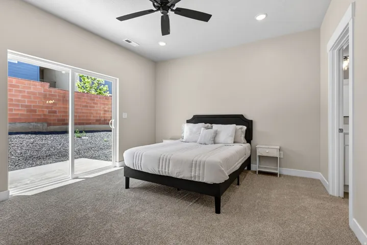 Carpeted bedroom with sliding glass door access to an exterior gravel patio area and a red brick retaining wall
