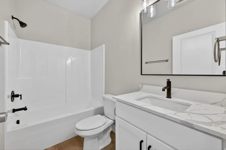 Bathroom featuring a white vanity with a white countertop and integrated sink, a frameless mirror, and a white tub with a shower