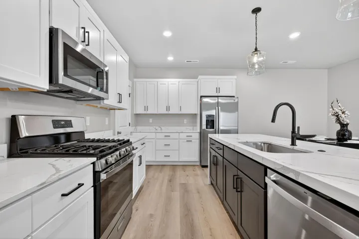 Kitchen featuring stainless steel appliances, white cabinetry, a central island with a sink, white countertops, and wood-finish flooring