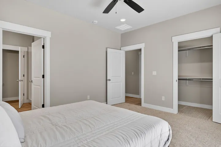 Bedroom featuring neutral gray walls, plush carpet flooring, a ceiling fan, white trim, and a closet with built-in shelving