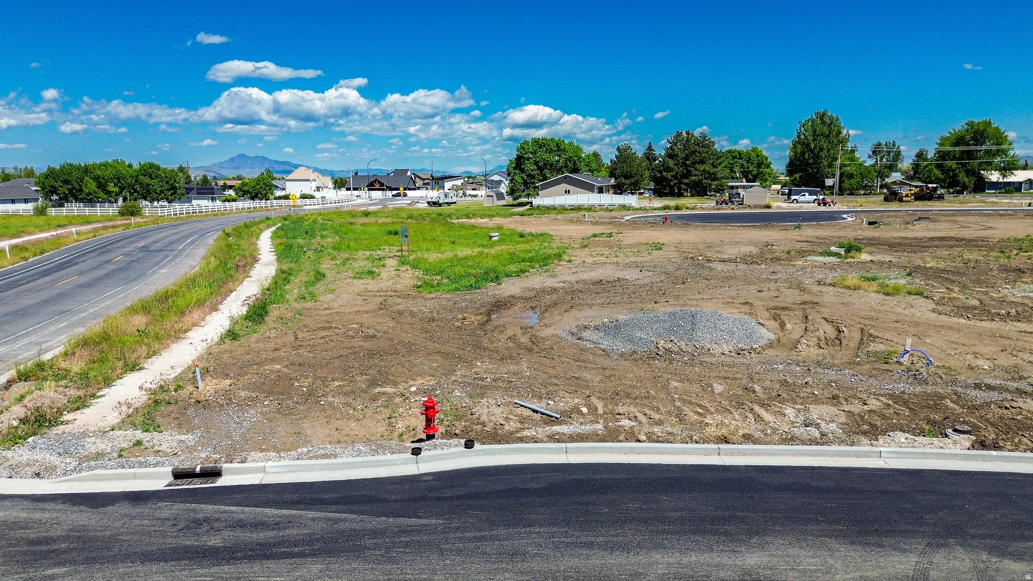 Expansive parcel featuring a newly paved road, curb, and visible utilities, with distant mountain scenery under a clear sky