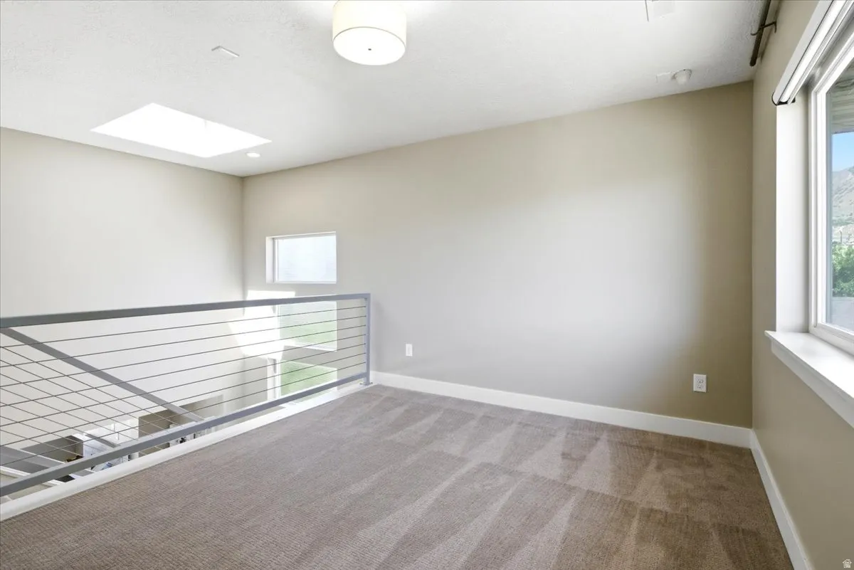 Carpeted loft area with a modern cable railing system, recessed lighting, and a large skylight