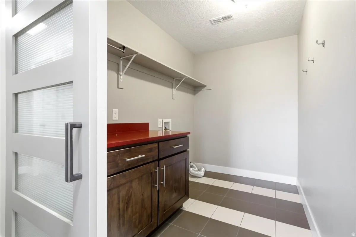 Laundry area featuring a dark wood-finish cabinet with a red countertop, white wall shelving, and wall-mounted hooks