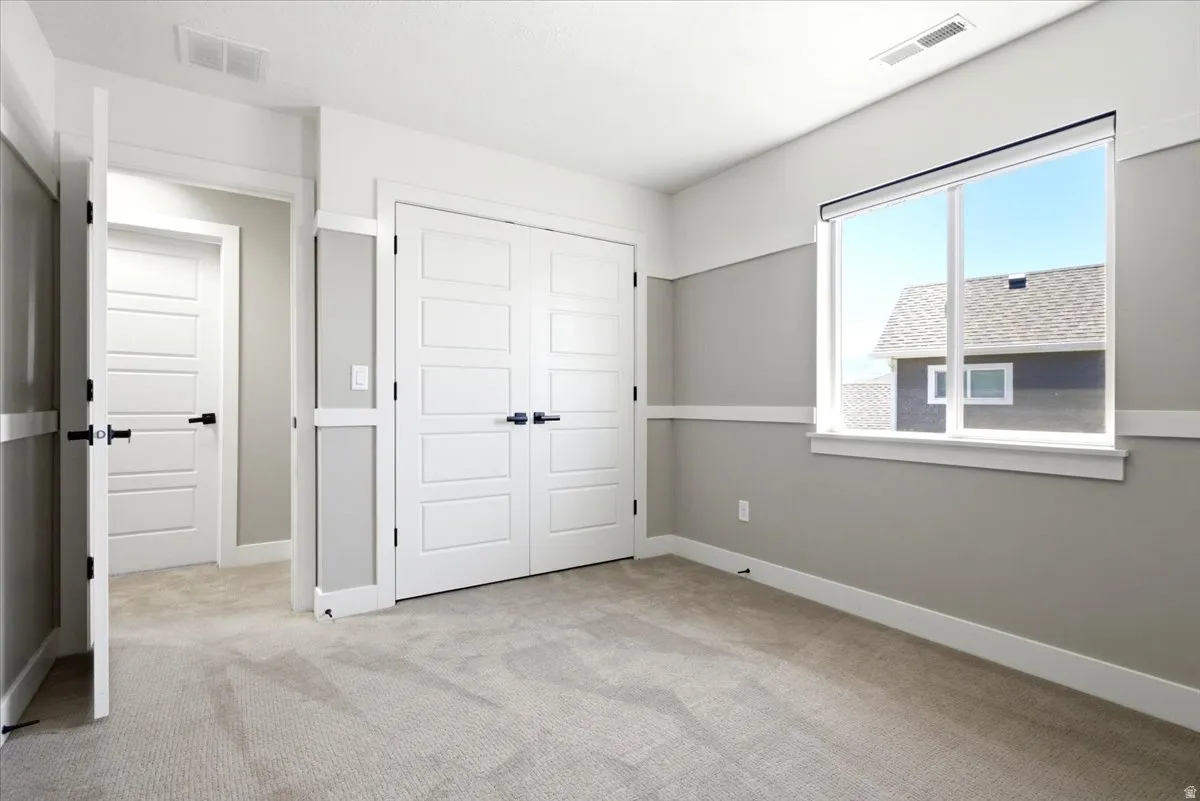 Carpeted room with a large window, white trim accents, light grey wall paint, and double white paneled closet doors with black hardware