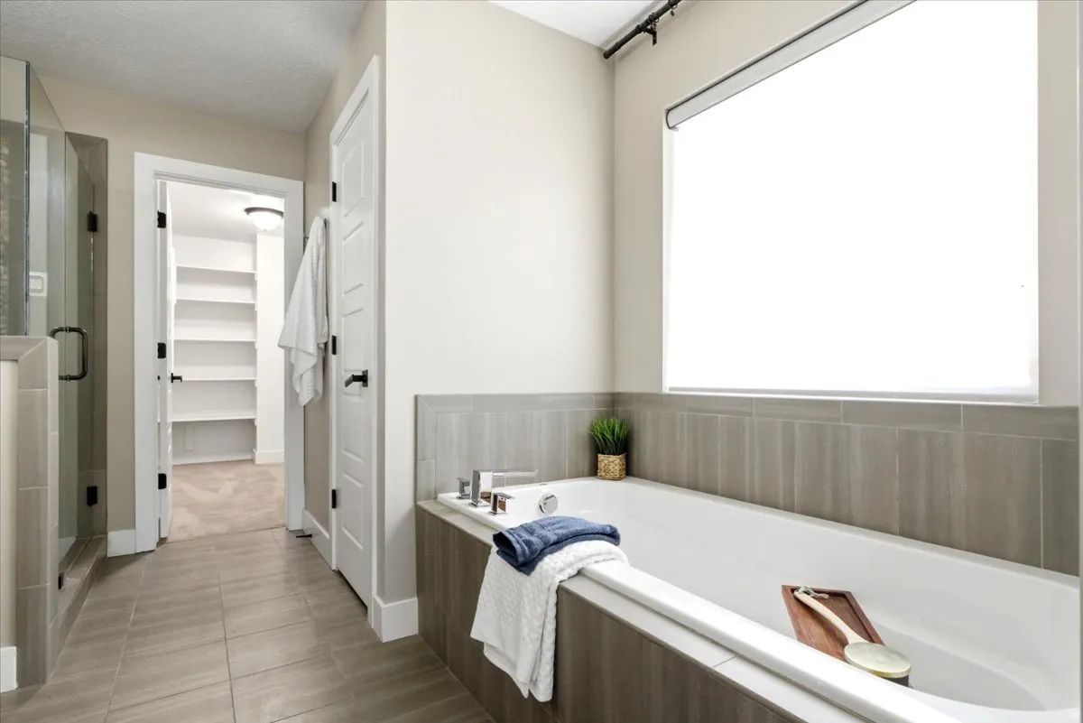 Bathroom featuring a built-in soaking tub with surrounding tile, a frameless glass shower enclosure, and wood-finish tile flooring
