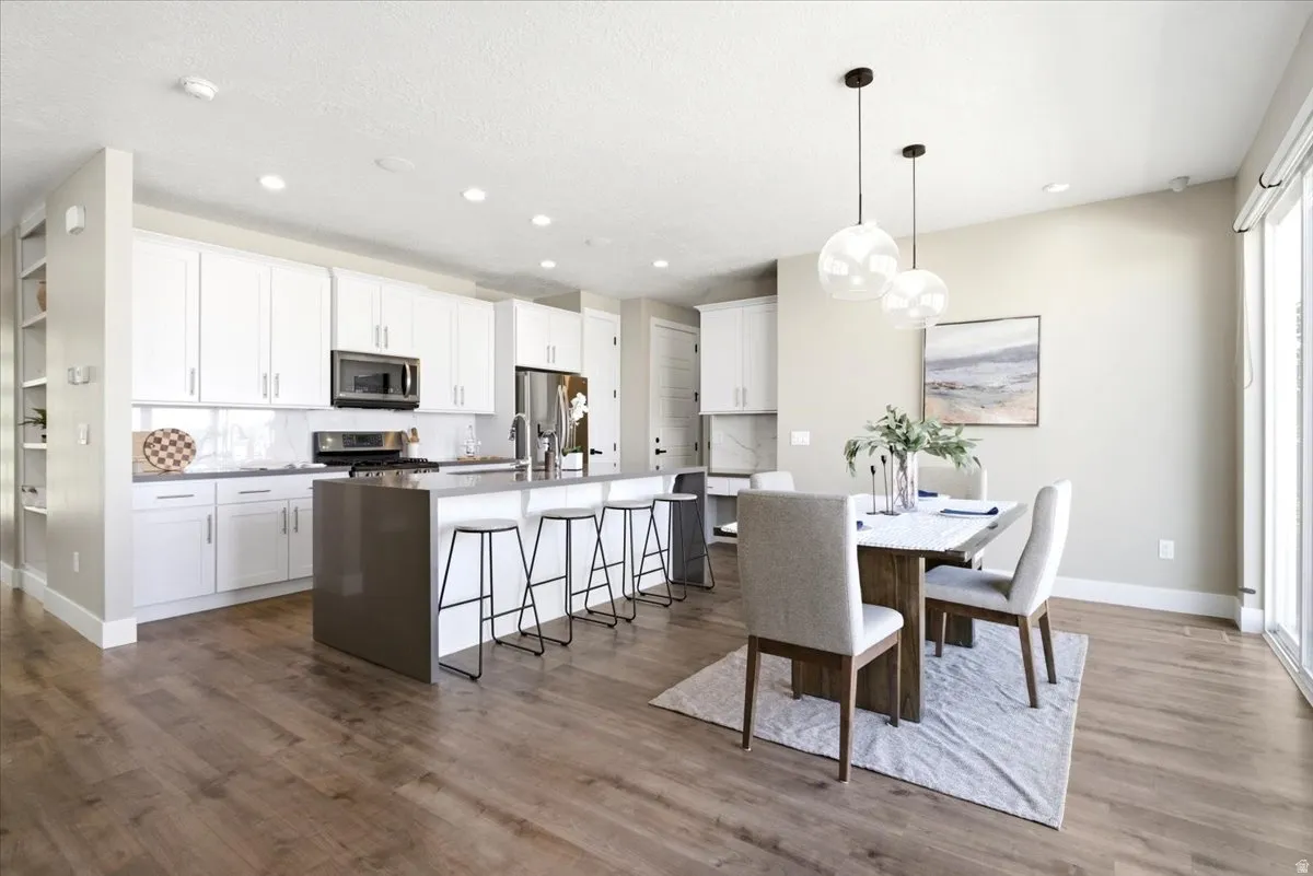Kitchen and dining area featuring wood-finish flooring, white cabinetry with silver hardware, and an island with bar seating