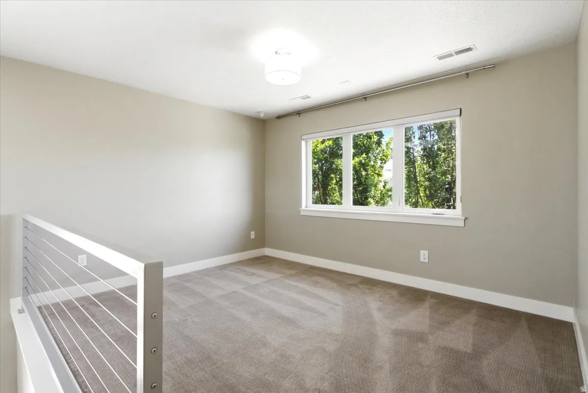 Carpeted interior space featuring a multi-pane window, modern cable railing, and a flush-mount ceiling light fixture